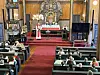 Prest ved alteret i en kirke med røde benker og tilskuere i benkeradene.