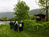 Gruppe vandrere med ryggsekker står ved en innsjø omgitt av grønn vegetasjon.
