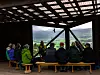 Personer sitter under et tak og ser ut over et landskap med fjell og grønn dal.
