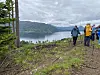 Turgåere på en skogkledd høyde med utsikt over fjord og fjell under grå himmel.