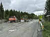 Anleggsmaskiner står ved en avsperret grusvei i skogsterreng.