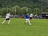 Flere fotballspillere løper etter ballen på en grønn gressbane med skog og publikum i bakgrunnen.