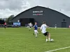 Fotballspillere spiller fotball på en gressbane foran en stor mørk hall.