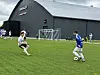 To spillere møter hverandre på en fotballbane foran en stor mørk hall.