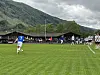 Fotballspiller i blått tar frispark på en grønn bane med fjell i bakgrunnen.