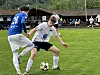 To fotballspillere kjemper om ballen på en gressbane foran publikum og en liten tribune.