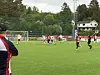 Fotballspillere i røde og hvite drakter på en gressbane sett fra sidelinjen.
