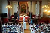 En fullsatt kirke med mennesker sittende i benker mens presten ber for konfirmantene, en og en.