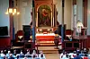 Prest ved alteret i en kirke med gullrammet maleri og menighet på benker i forgrunnen.