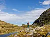 En person står på en steinrygg i et fjellandskap med vann og bratte fjellsider.