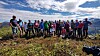 En stor gruppe turgåere står samlet på en fjellrygg med utsikt over landskapet.