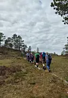 En gruppe turgåere går i rekke langs en sti i et gresskledd, kupert landskap.