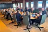 Gruppe samlet rundt et langt bord i et møterom med skjermer, papirer og kaffekopper.