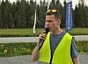 En mann med refleksvest snakker i mikrofon utendørs  og skog i bakgrunnen.