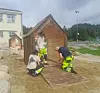 Tre personer monterer et lite trehus på en lekeplass ved en boligblokk.