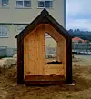 Lite trekledd hus plassert foran en boligblokk på en byggeplass.