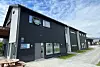 Mørkt moderne bygg med store vinduer ved en asfaltert vei og delvis skyet himmel.