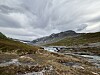 Elv som renner gjennom et steinete fjellområde under mørke skyer.