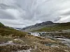 Elv som renner gjennom et steinete fjellområde under mørke skyer.