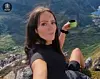 Kvinne sitter på en stein i fjellet og holder en kopp med utsikt over dalen.