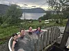 Fire personer tar et utendørs karbad med utsikt over fjord, fjell og landskap. Kyr på åkeren bak.