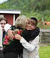 To personer omfavner hverandre utendørs, med en tredje person delvis synlig i bakgrunnen.