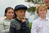 Barn står utendørs foran en uskarp bakgrunn, ett med caps i midten.