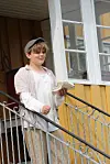 Gutt står i trappen foran et gult hus og holder to grytekluter.