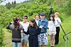 Åtte barn står samlet utendørs foran et kamera i en grønn park.