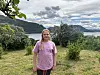 Jente i rosa T-skjorte står foran et grønt landskap med fjord og fjell.