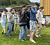 Barn i rekker på gresset danser ved en gul bygning.