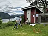 Barn leker på gresset ved et rødt hønsehus med fjorden i bakgrunnen.