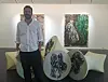 En mann står ved siden av store, runde kunstverk i et galleri med to malerier på veggen.