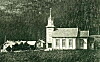 Historisk kirke med tårn og små bygninger i et landlig område.