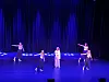 Fire dansere på en scene foran mørke gardiner med blå scenebelysning.