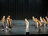 En gruppe dansere på en mørk scene foran et svart sceneteppe.