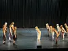 En gruppe dansere på en mørk scene foran et svart sceneteppe.