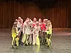 En gruppe dansere samlet midt på en scenegulv foran et brunt sceneteppe.