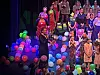 Mennesker står på en scene omgitt av mange fargerike ballonger i et opplyst scenemiljø.