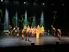 Flere dansere og skuespillere står på en opplyst scene med mørk bakgrunn og grønne lysdetaljer.