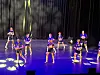 Flere dansere står og poserer på en scene med blått lys og mørk bakgrunn.