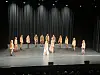 En gruppe dansere står på en mørk scene med svart teppebakgrunn og scenelys ovenfra.