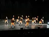 Flere dansere opptrer på en stor scene med mørk bakgrunn og scenelys.