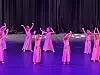 Dansere i rosa kjoler med armene løftet på en scene badet i lilla lys.