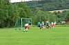 Fotballspillere samles foran målet på en gressbane i et landlig landskap.