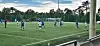 Fotballspillere i blå og hvite drakter spiller på en kunstgressbane ved et mål.