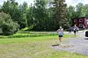 To løpere på en grusvei ved et skogkledd område, med en rød bygning i bakgrunnen.