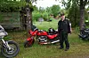 En mann står ved en rød motorsykkel på en gressplen omgitt av andre parkerte motorsykler.