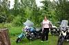 En kvinne står ved tre motorsykler i et grønt hageområde med trær i bakgrunnen.