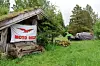 Provisorisk leir med telt, henger og skur med Moto Guzzi-banner i grønt skogsområde.